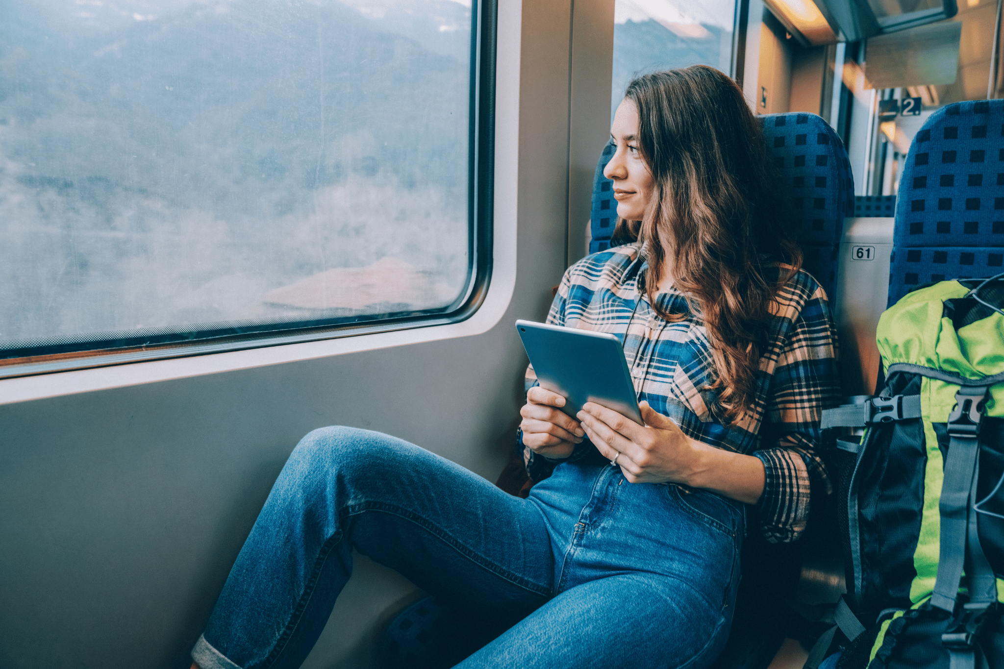 A woman sitting on a train holding her ipad because she is using travel apps to help her travel the world safely