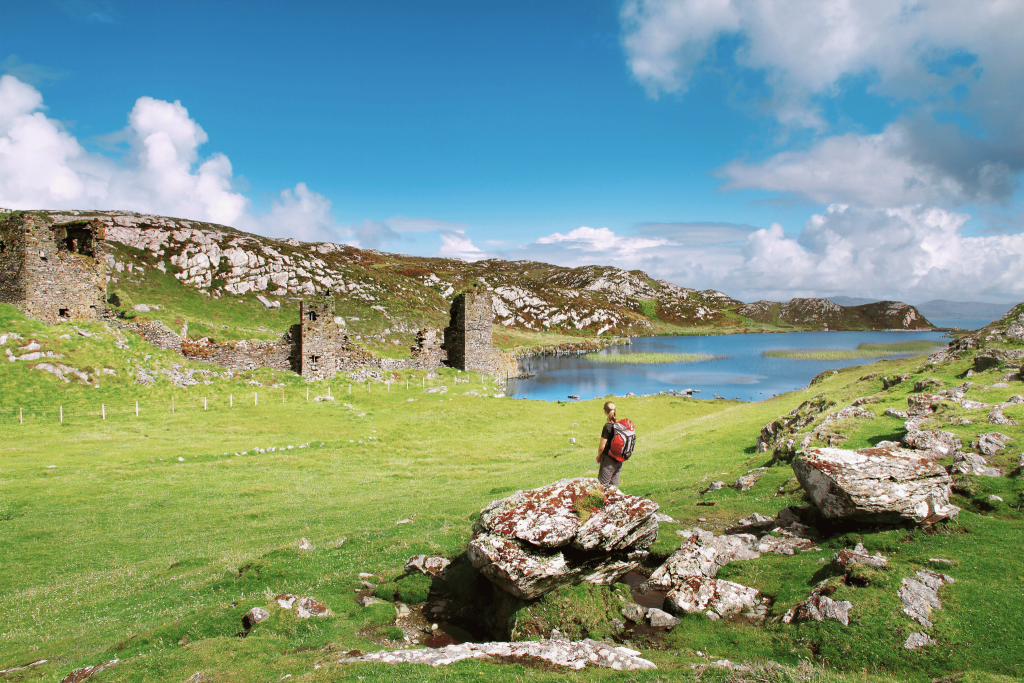 A woman hiking with a backpack in Ireland overlooking a beautiful green field and farmland
