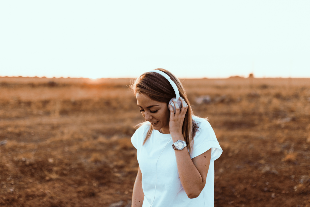 A woman in a field wearing headphones listening to travel songs to inspire her. Tengah