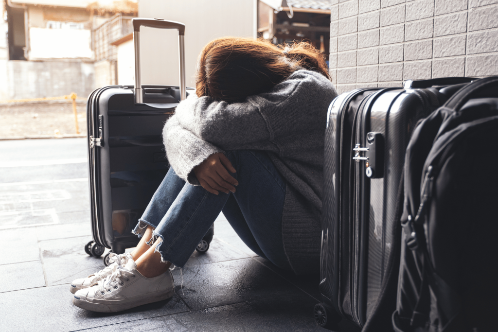 A girl sat on the ground with her head in her hands. She is surrounded by suitcases and is really sad. The Case Against Travel - why it's not for everyone.